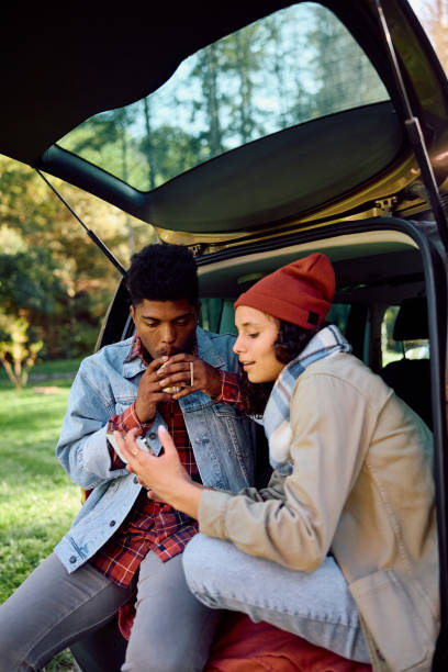 istock Young couple using smart phone while relaxing in car trunk in nature. 2181988974
