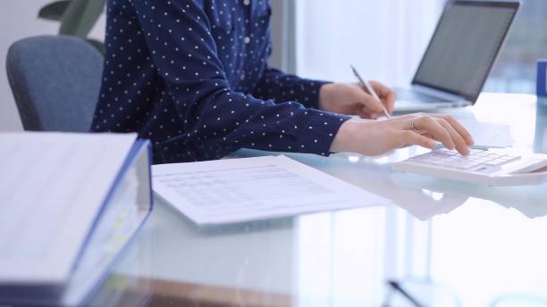 istock A female accountant with blue dotted blousy is using a laptop computer and calculator to calculate taxes at a glass desk in the office. Right side view 2181997274