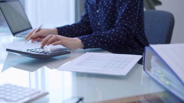 istock A female accountant with blue dotted blousy is using a laptop computer and calculator to calculate taxes at a glass desk in the office. Left side view 2181998336
