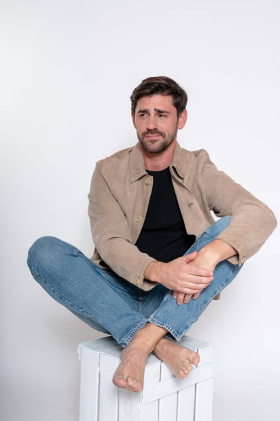 istock Pensive man sitting barefoot on white crate wearing casual clothes 2182002029