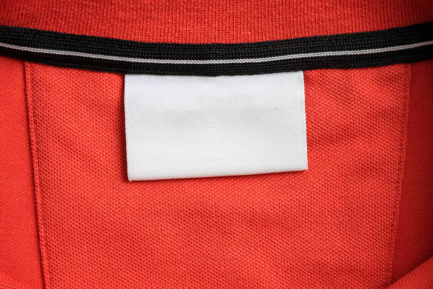istock Blank white laundry care clothes label on orange shirt fabric texture background 2182006686