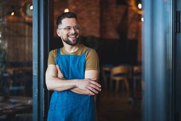 istock Smiling Man in Apron Standing in Cozy Cafe Entrance 2182007789