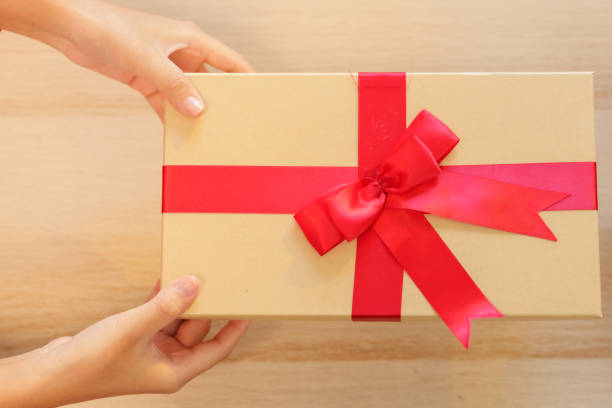 istock Hands holding a beautifully wrapped gift box with red ribbon and bow, symbolizing holiday generosity. Simple, minimalist style emphasizes thoughtfulness and festive spirit in holiday season. 2182009585