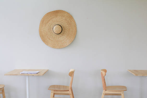 Wooden chairs and table in bright modern interior with wicker big hat on white wall.  Minimal living room.