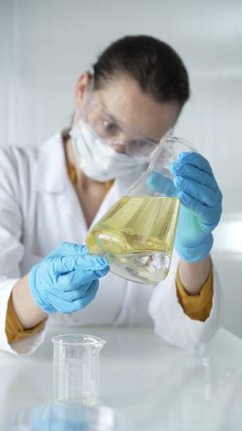istock Woman scientist, wearing a lab coat, blue protective gloves, is holding an Erlenmeyer flask with yellow oily liquid in laboratory setting, portrait and vertical view. Medicine, science concept 2182014130