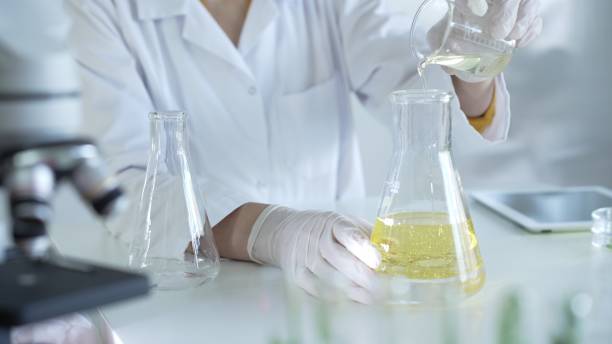 istock A scientist, wearing a lab coat and white protective gloves, is pouring a yellow oily liquid from one beaker to another near microscope in laboratory, close up. Medicine and science concept 2182015952