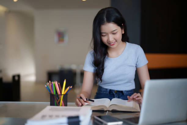 istock Asian teenage student woman reading a book and writing notes to doing homework while watching lecture video online lesson on digital laptop to studying and learning about education knowledge in cafe 2182020885