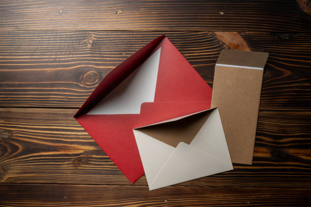 Top view of stack of three envelope and postcard on wooden background. The envelopes are of different variation size and colors. Mockup, blank template, copy space. Greeting or invitation card with flat lay style