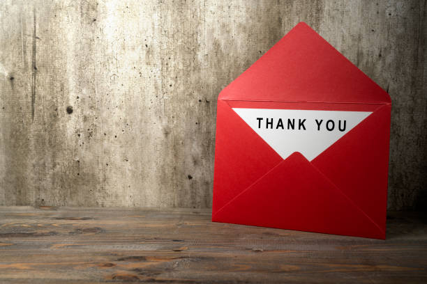 Red envelope and postcard with white card with words Thank You written on it on the table