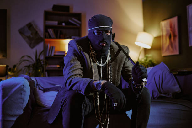 Portrait of unrecognizable thief in jacket and golden pearl necklaces holding metal crowbar and looking at camera