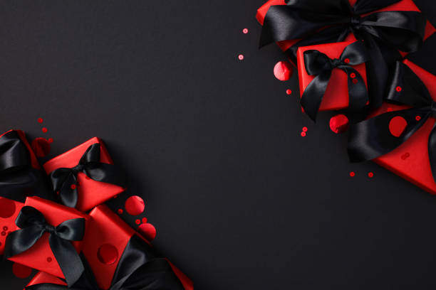 istock Black Friday sale concept. Elegant luxury gift boxes with black ribbons on a dark background, highlighted by red confetti. 2182043924
