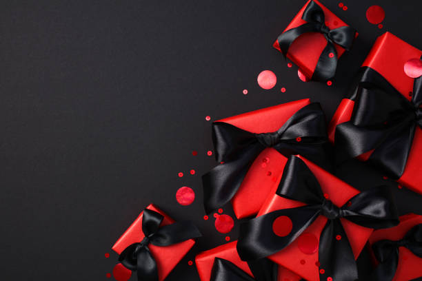 istock Black Friday sale discount concept. Elegant red gift boxes with black bows on a dark backdrop, surrounded by festive red confetti 2182043978
