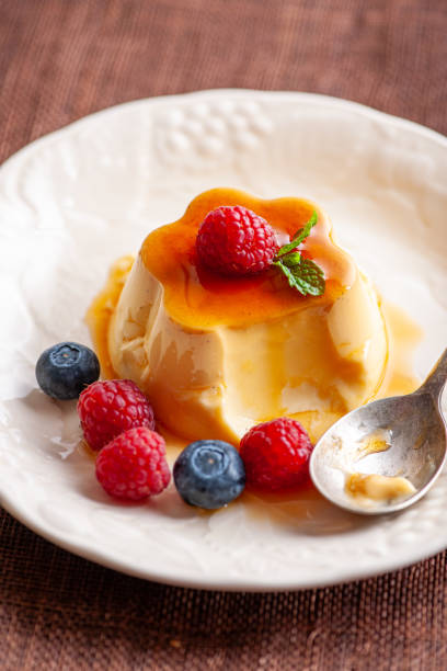 Caramel flan dessert garnished with fresh raspberries, blueberry, and mint