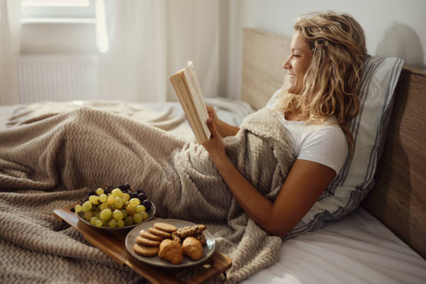 Happy woman reading a book during morning in a bed.
