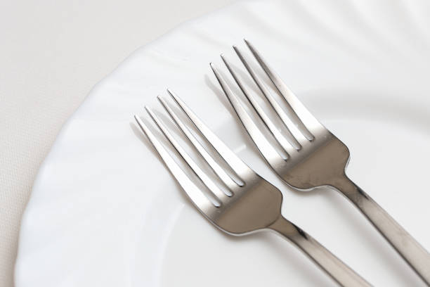 istock Silver cutlery background. White tablecloth with ceramic plate. Two forks elegant dishware. Dining at restaurant. 2182050527