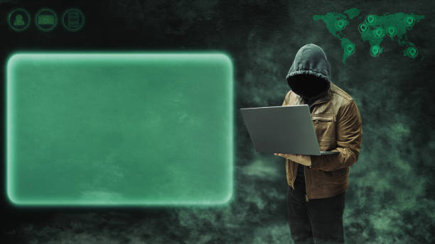 istock Faceless, anonymous hacker in a hoodie and leather jacket, standing with a laptop against a dark background with empty space for text. Copy space 2182052313