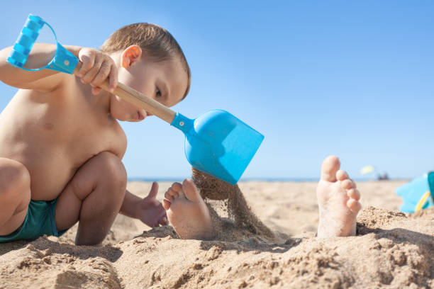 Toddler throws sand on his brother's feet with a shovel