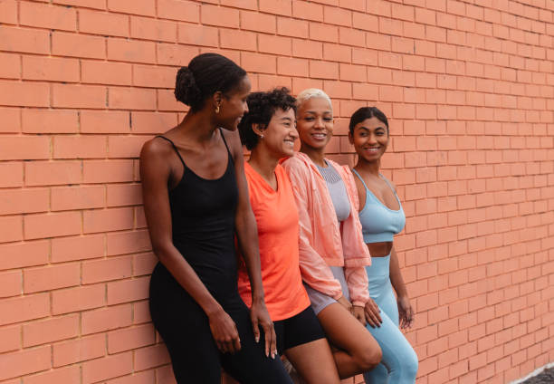 istock Four sportswomen leaning against a brick wall smiling and relaxing after training 2182064376