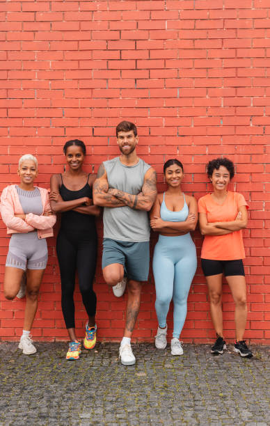 Five smiling athletes with crossed arms standing against a red brick wall in the city after training, enjoying their active lifestyle and teamwork