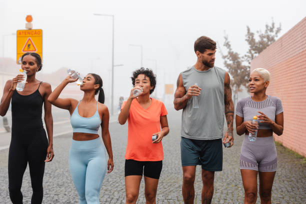 Athletes hydrating after workout in city, showing dedication to fitness. Urban setting adds dynamic backdrop to active lifestyle. Candid moment captures strength and progress in fitness goals