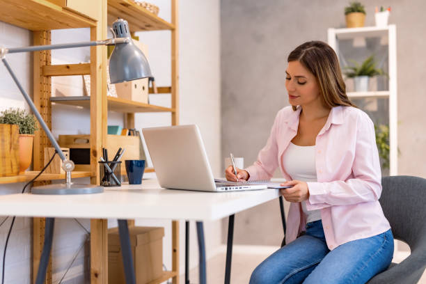 istock Woman writing notes next to laptop in home setting 2182067896