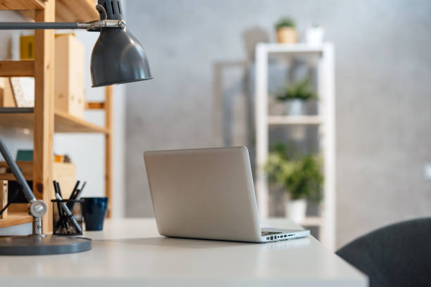 A minimalist home office setup featuring a sleek laptop on a white desk, accompanied by modern metallic lighting, perfect for productivity in a serene environment.