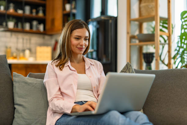 istock Smiling woman on couch typing on silver laptop 2182068114