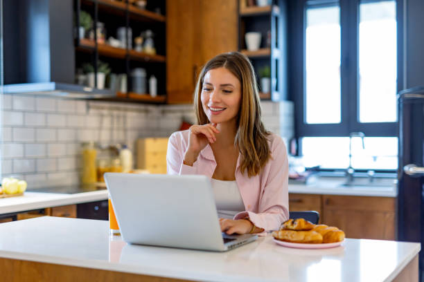 istock Happy woman works on laptop in sunny kitchen space. 2182068274