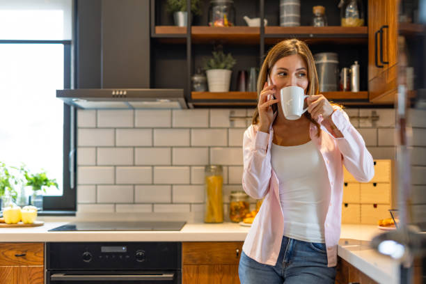 istock Woman enjoys drink in stylish kitchen while calling 2182068461