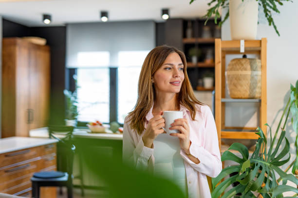 Relaxed woman holding mug near kitchen area, smiling.