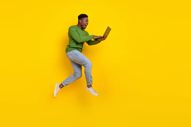istock Full length body size view of attractive cheery guy jumping using laptop web order buy isolated over vivid yellow color background 2182072933