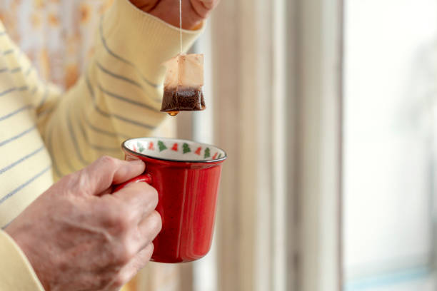 istock Person holding red mug with Christmas decorations on rim, dipping tea bag while droplet hangs from bag in warm, softly lit setting 2182076031