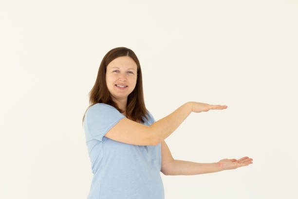 istock Young confident woman showing logo on empty space between arms. Smiling girl inviting or advertising promo deal, pointing hands right and looking at camera, white background. 2182078050