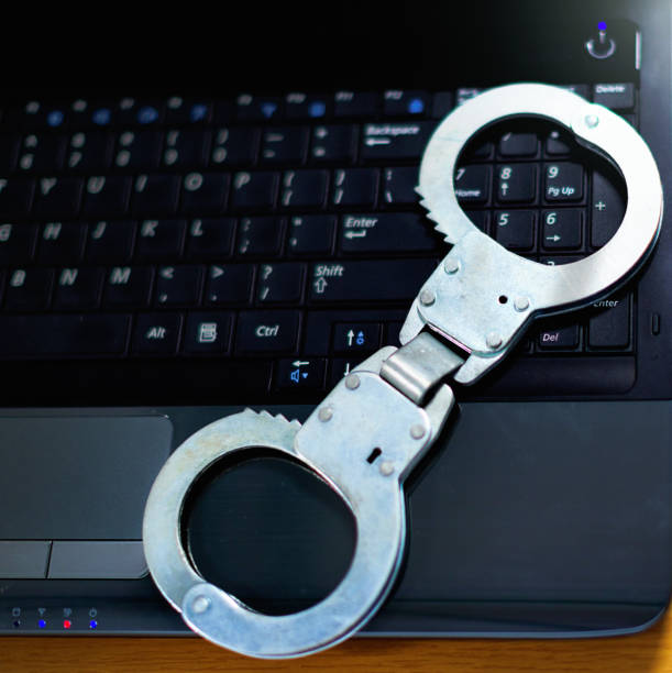 Shiny metal handcuffs on the keyboard of a laptop computer.