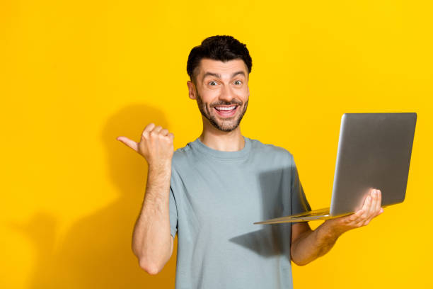 istock Photo of young successful programmer student man hold laptop finger directing empty space excited new startup offer isolated on yellow color background 2182084445