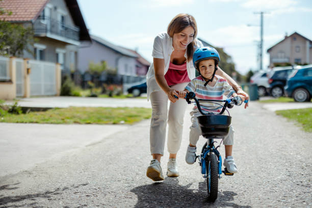 istock Mother Teaches Boy to Ride a Bicycle on the Sidewalk 2182089648