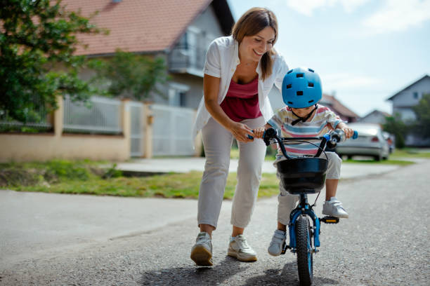 istock Mother Teaches Boy to Ride a Bicycle on the Sidewalk 2182089653