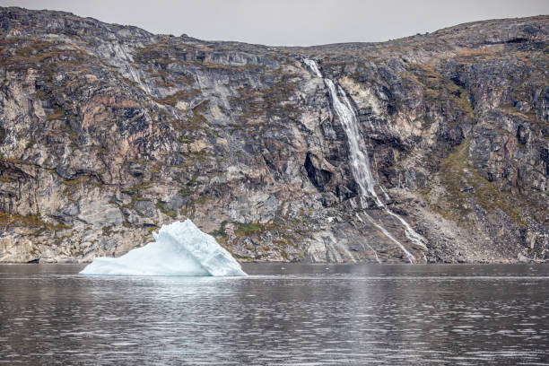 Iceberg floating on calm water in front of a barren rock wall in a fjord outside Ilulissat in western Greenland which is an UNESCO World Heritage Site due to the Ice Fjord