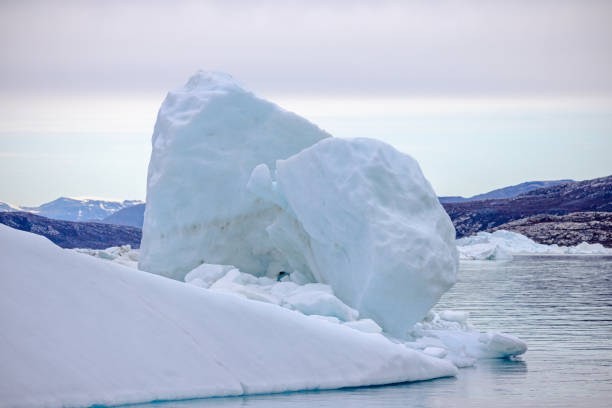 Iceberg floating on calm water in front of a barren rock wall in a fjord outside Ilulissat in western Greenland which is an UNESCO World Heritage Site due to the Ice Fjord