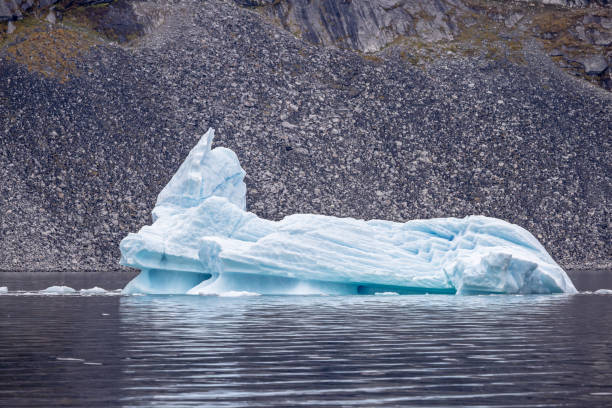 Iceberg floating on calm water in front of a barren rock wall in a fjord outside Ilulissat in western Greenland which is an UNESCO World Heritage Site due to the Ice Fjord