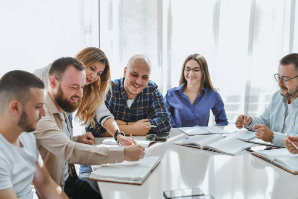 istock Female Professor Checking Male Student's Handwriting While Other Students are Smiling and Looking Happy 2182098428