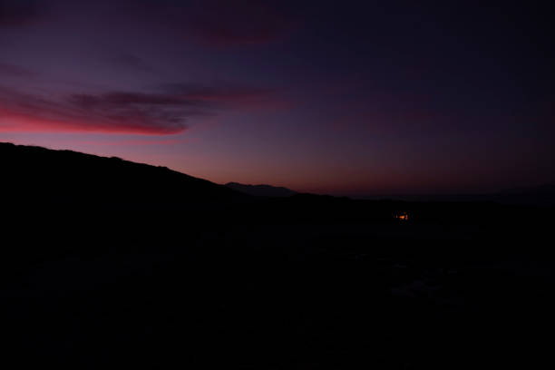 Sand dunes forming a dark silhouette against a colorful gradient sky during twilight, creating a minimalist and serene desert landscape