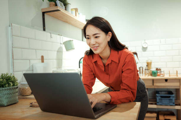 istock Smiling well dressed woman using laptop in a domestic kitchen 2182109619