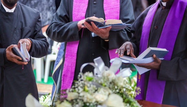istock three priests reading prayers from the bible at a funeral to bless the grave, 2182112466