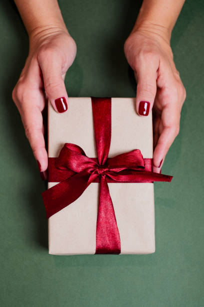 istock Womans hands holding a wrapped Christmas gift on green surface. 2182112722