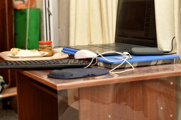 Work clutter on a home desk, laptop and breakfast tray.