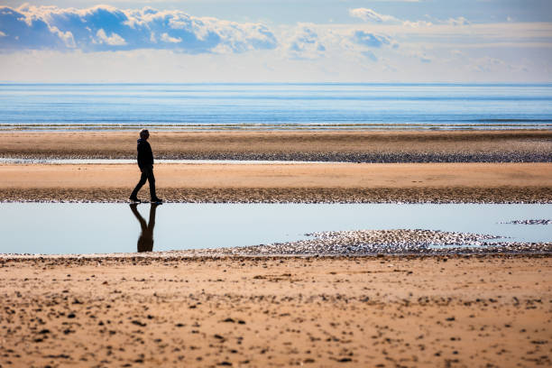 istock Senior man walking on sandy beach alone with calm sea and cloudscape 2182117529