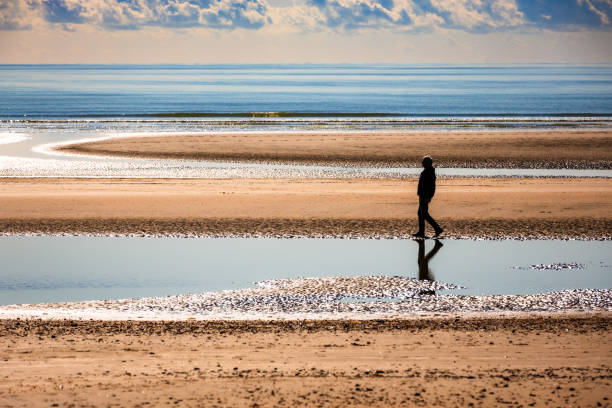 istock Senior man walking on sandy beach alone with calm sea and cloudscape 2182117546