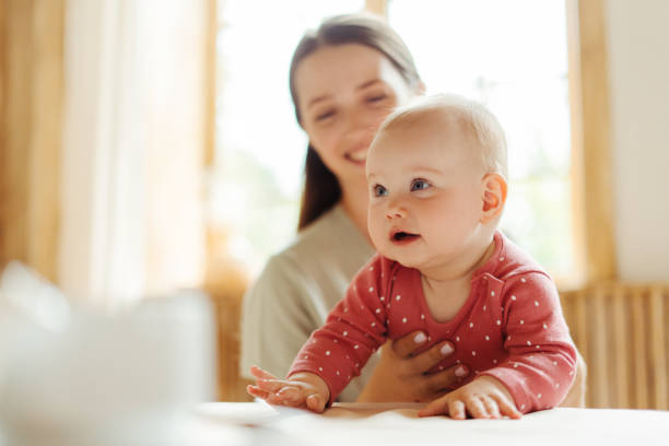 Baby girl exploring table with mother supporting her