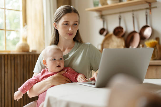 istock Mother working from home holding her baby and using laptop computer 2182118481